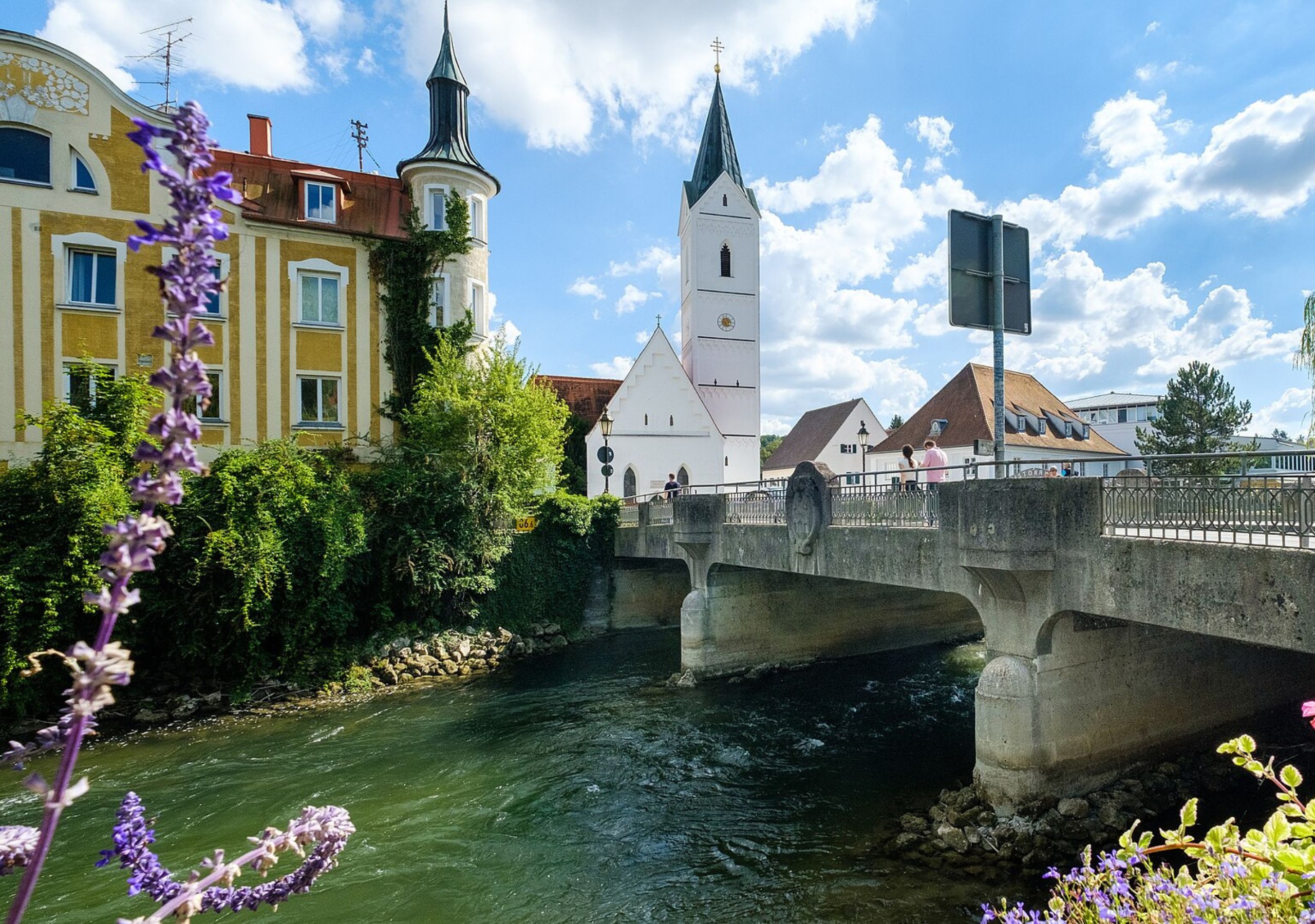 Fluss mit Brücke und Kirchturm im Hintergrund.